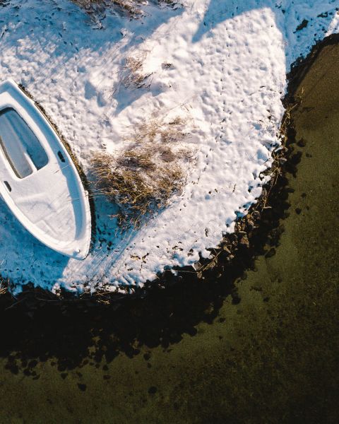 Blick von oben auf eine verschneite, kleine Halbinsel mit Boot