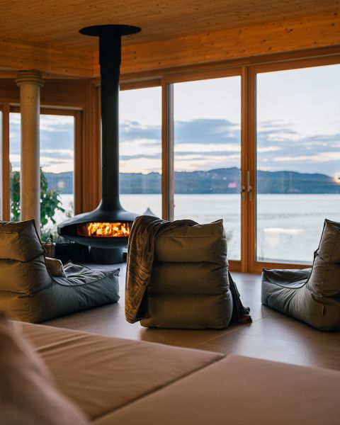 Gemütliche Liegen im Raum der Luft vor dem Kamin mit großen Panoramafenstern und Blick auf den See