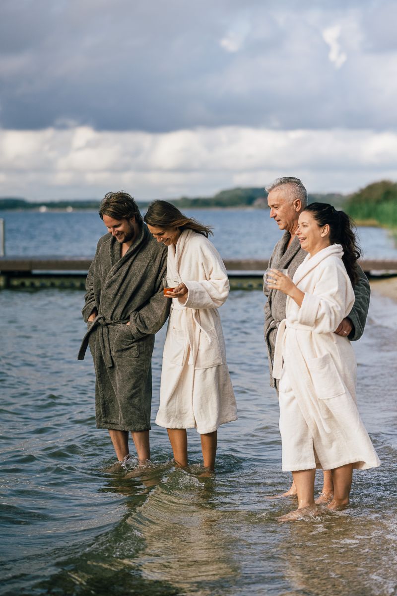 Gruppe in Bademänteln am Strand mit den Füßen im Wasser