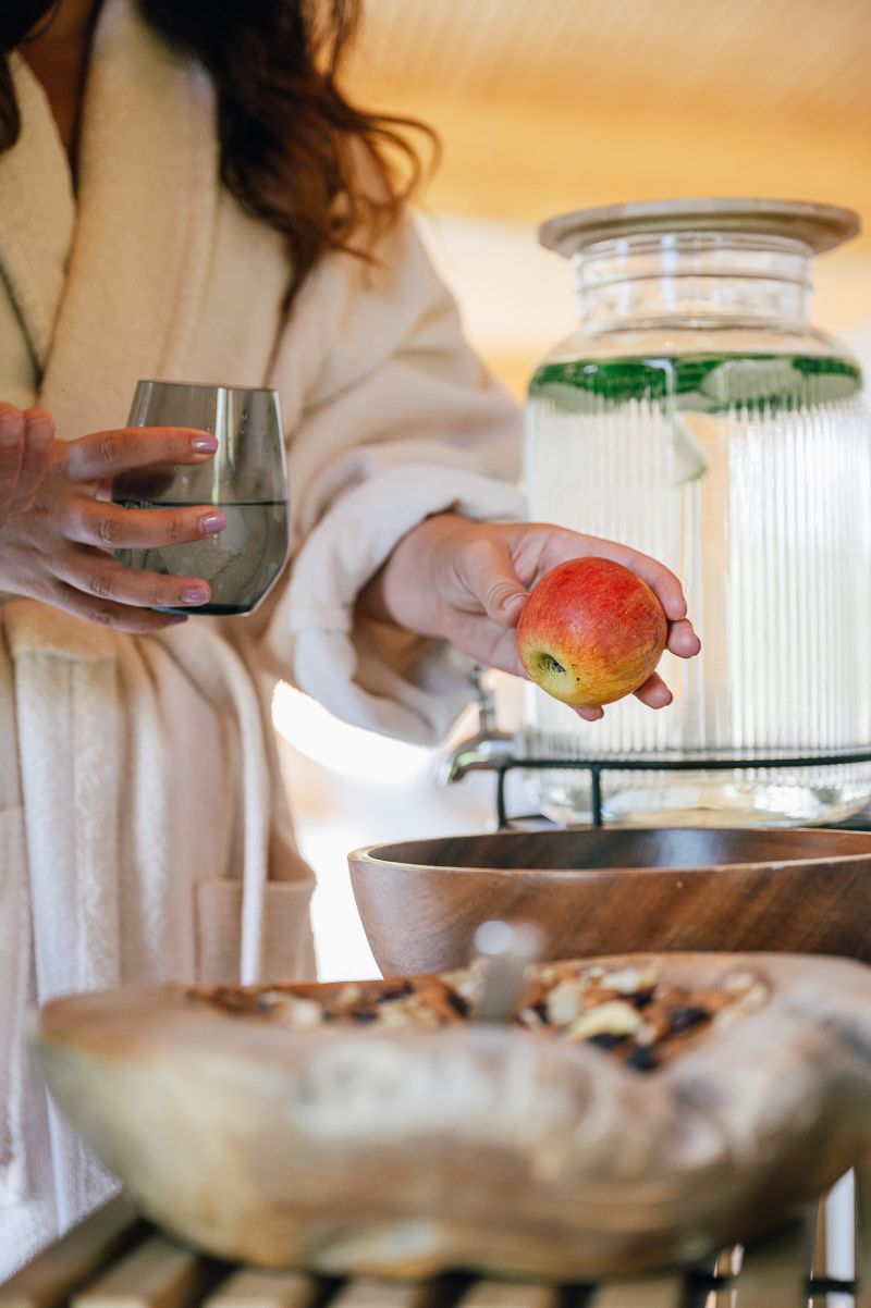 eine Dame nimmt sich ein Apfel und ein Glas Wasser von der Snackstation in einem Rueraum