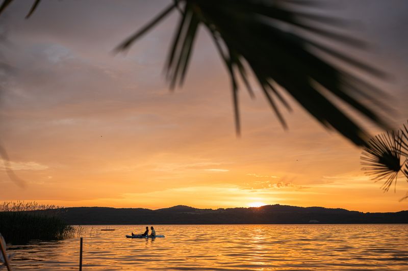 Blick auf die untergehende Sonne und ein Pärchen auf einem SUP