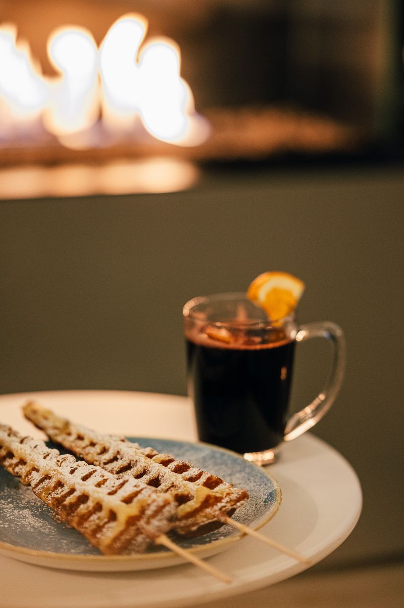 Glühwein und hausgemachte Waffeln auf einem Tisch vor dem brennenden Kamin im Glaspavillon