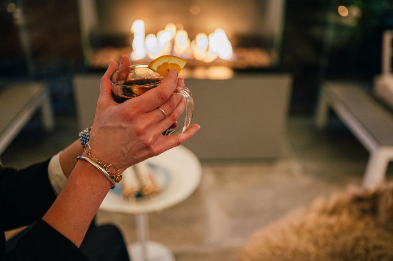 Hände halten ein Glühweinglas im Hintergrund der Kamin