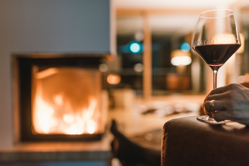 Frau sitzt in der Bibliothek mit einem Glas Wein in der Hand vor dem Kamin
